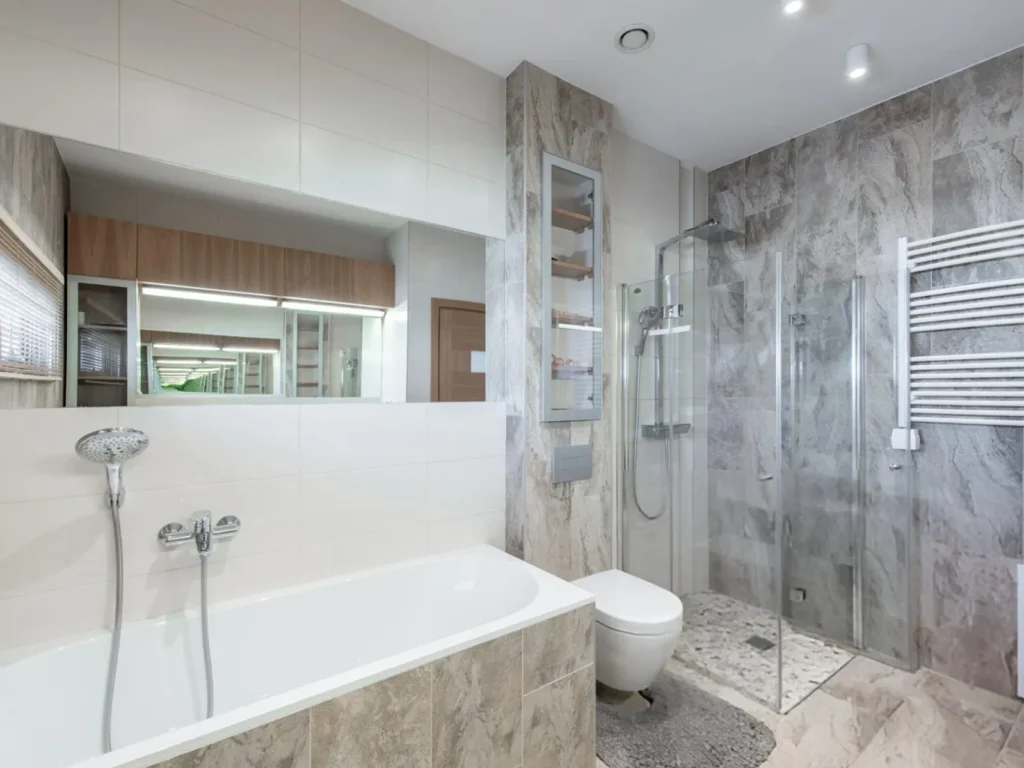 Full bathroom renovation by ATM Renovations featuring custom grey marble wall tiles, a built-in bathtub, a glass walk-in shower, and a wall-hung toilet.
